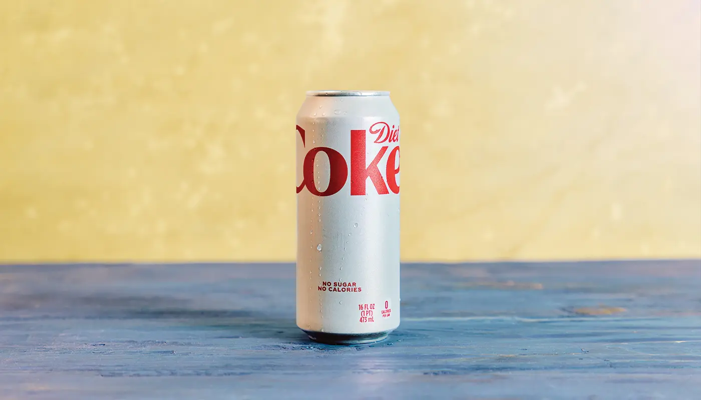 A Diet Coke can on blue wooden boards against a yellow wall.