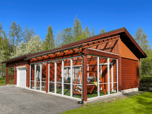 Ulkomaalattu puinen autotalli ja lasitettu lisäsiipi Vimpelissä, lämpimän punaruskea sävy ja huoliteltu ympäristö