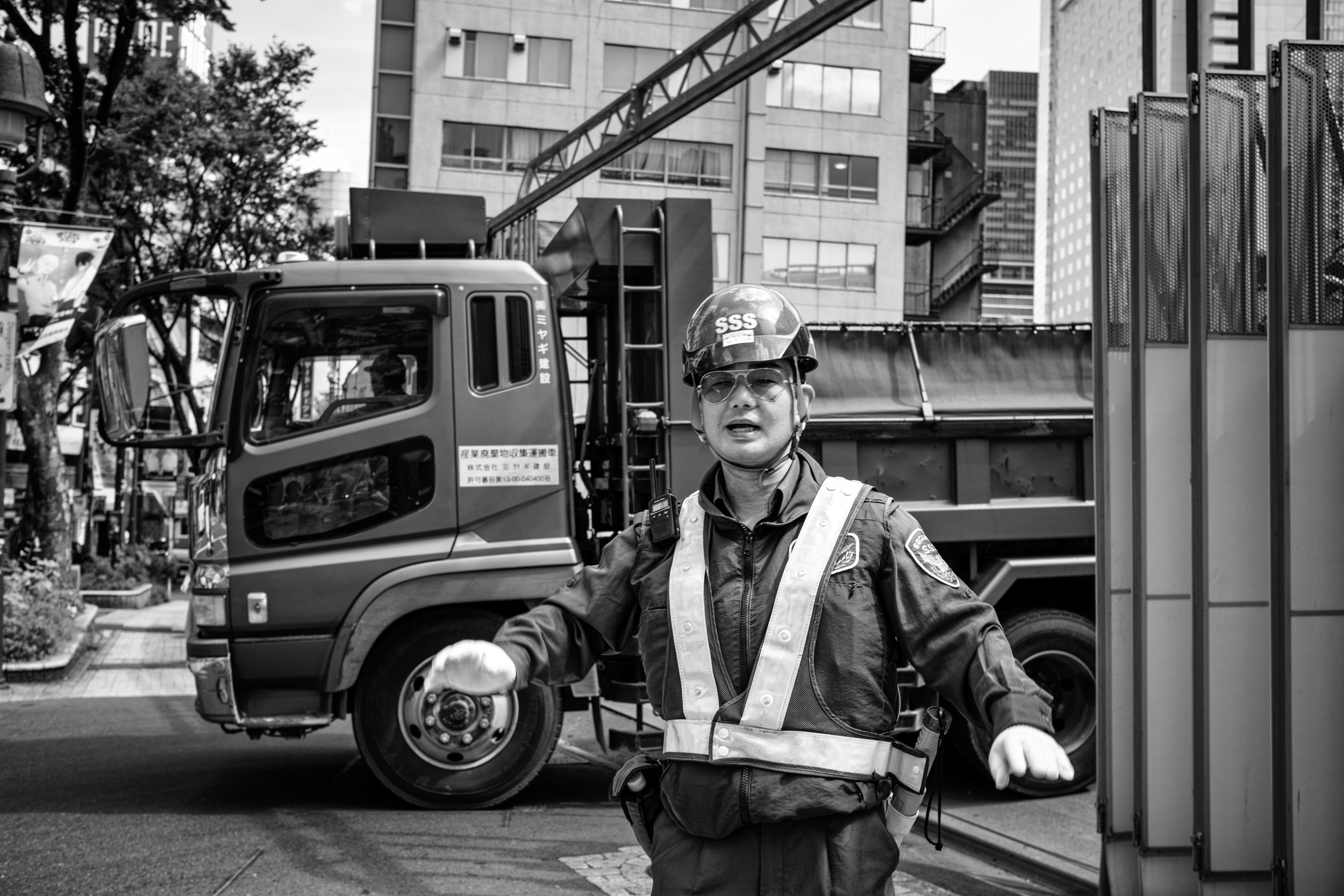 Black and white street photograph of a construction worker directing traffic beside a truck.