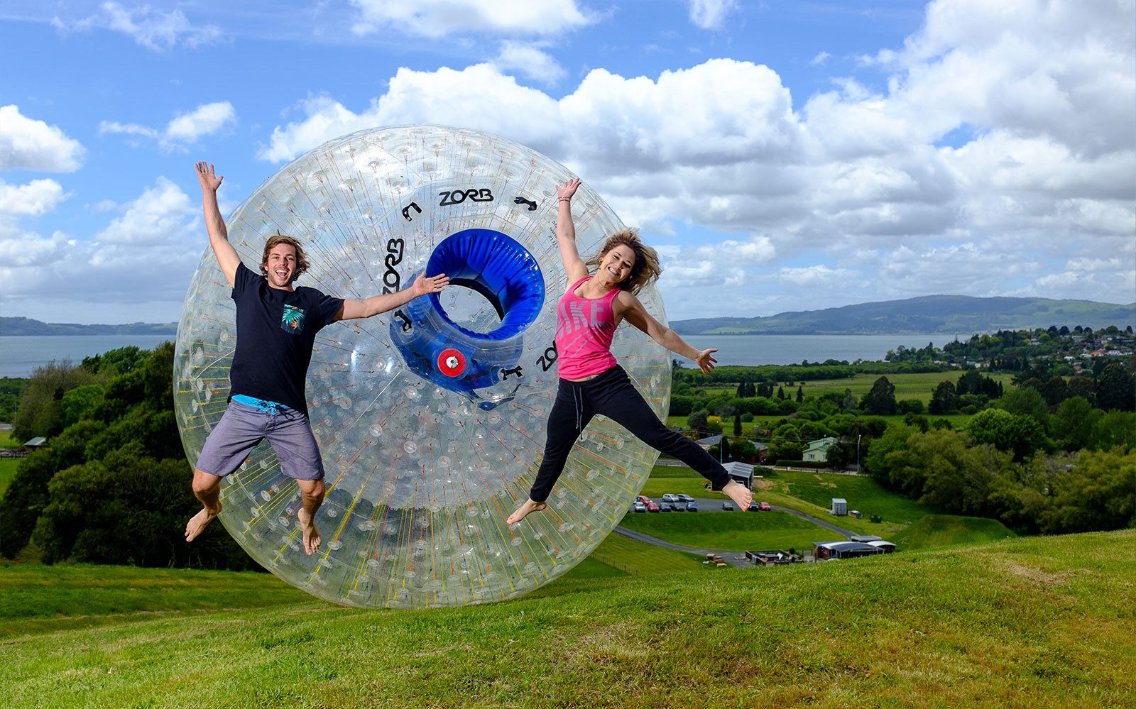 People enjoying Zorb Rotorua VIP Experience on a grassy hill with scenic lake view.