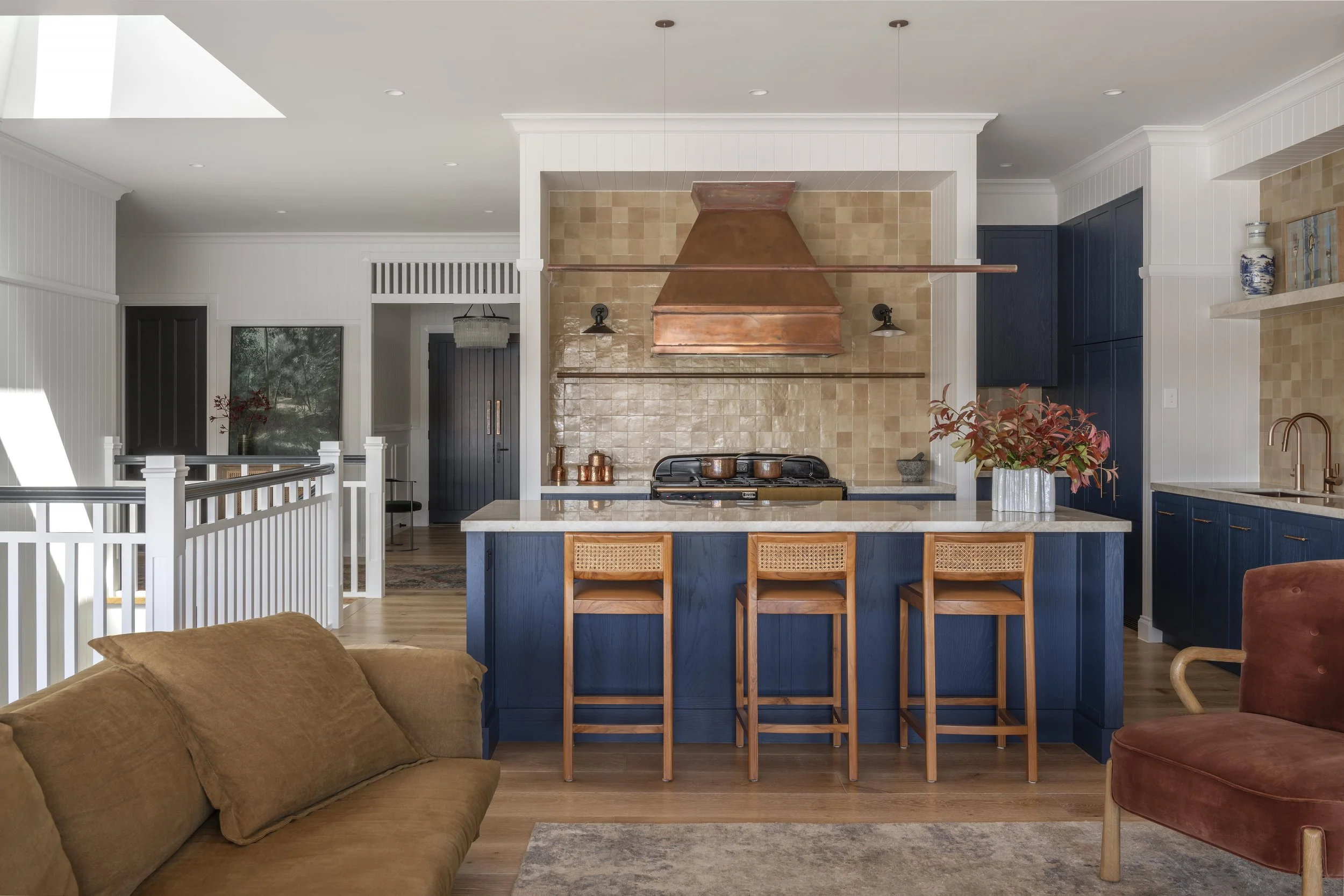 Open-plan kitchen with navy island, copper range hood, and warm tiled splashback.