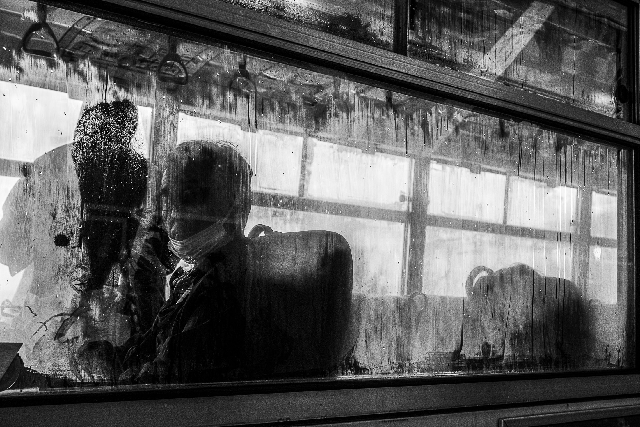 Black and white photograph of a passenger seen through a bus window covered with condensation, street photography by Richard Peterson.
