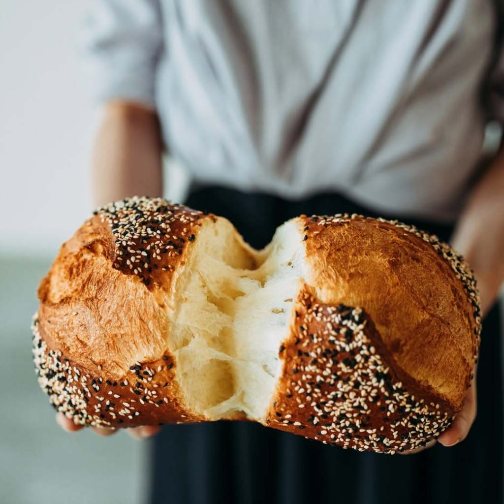 A close-up of a person holding a freshly baked sesame-seed topped sourdough loaf, showing its soft and light interior.