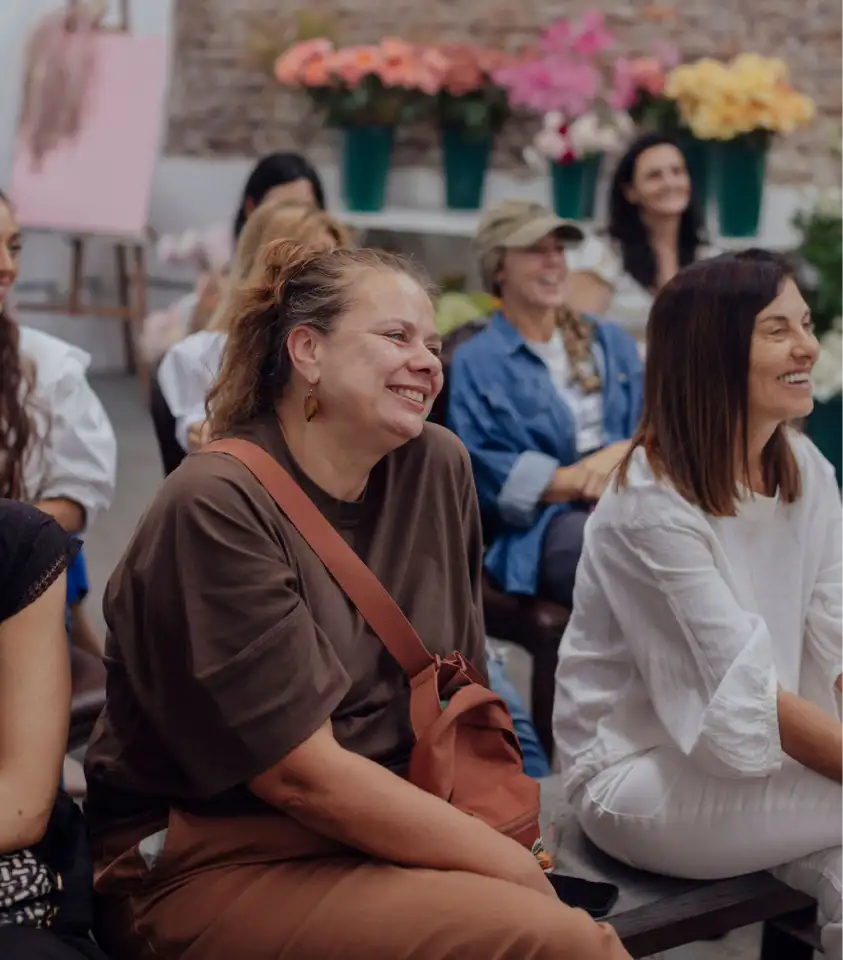 Grupo de mujeres sonriendo y participando en un taller floral, ambiente distendido y comunitario.