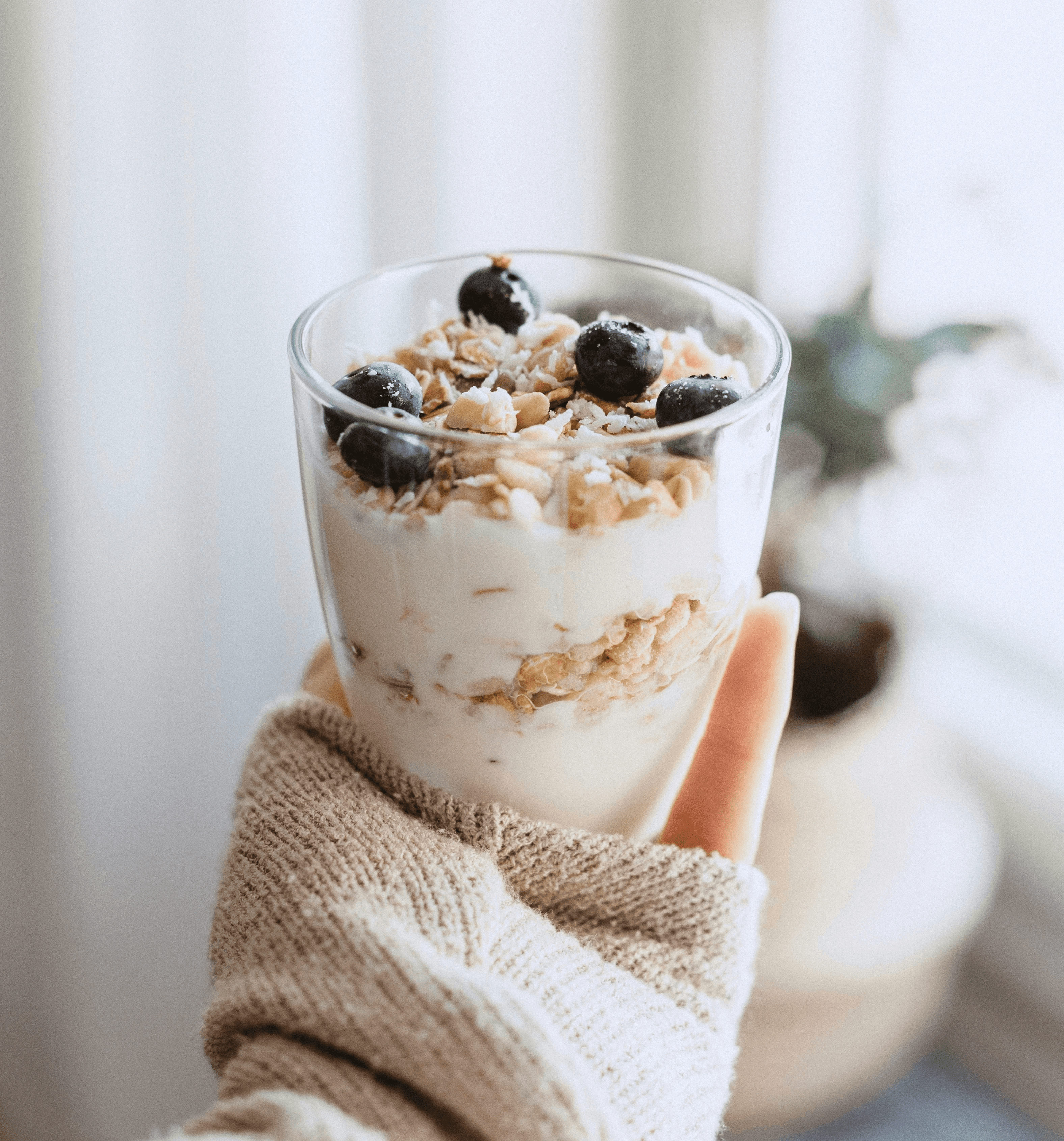 A hand holding a glass filled with muesli, blueberries and yoghurt.