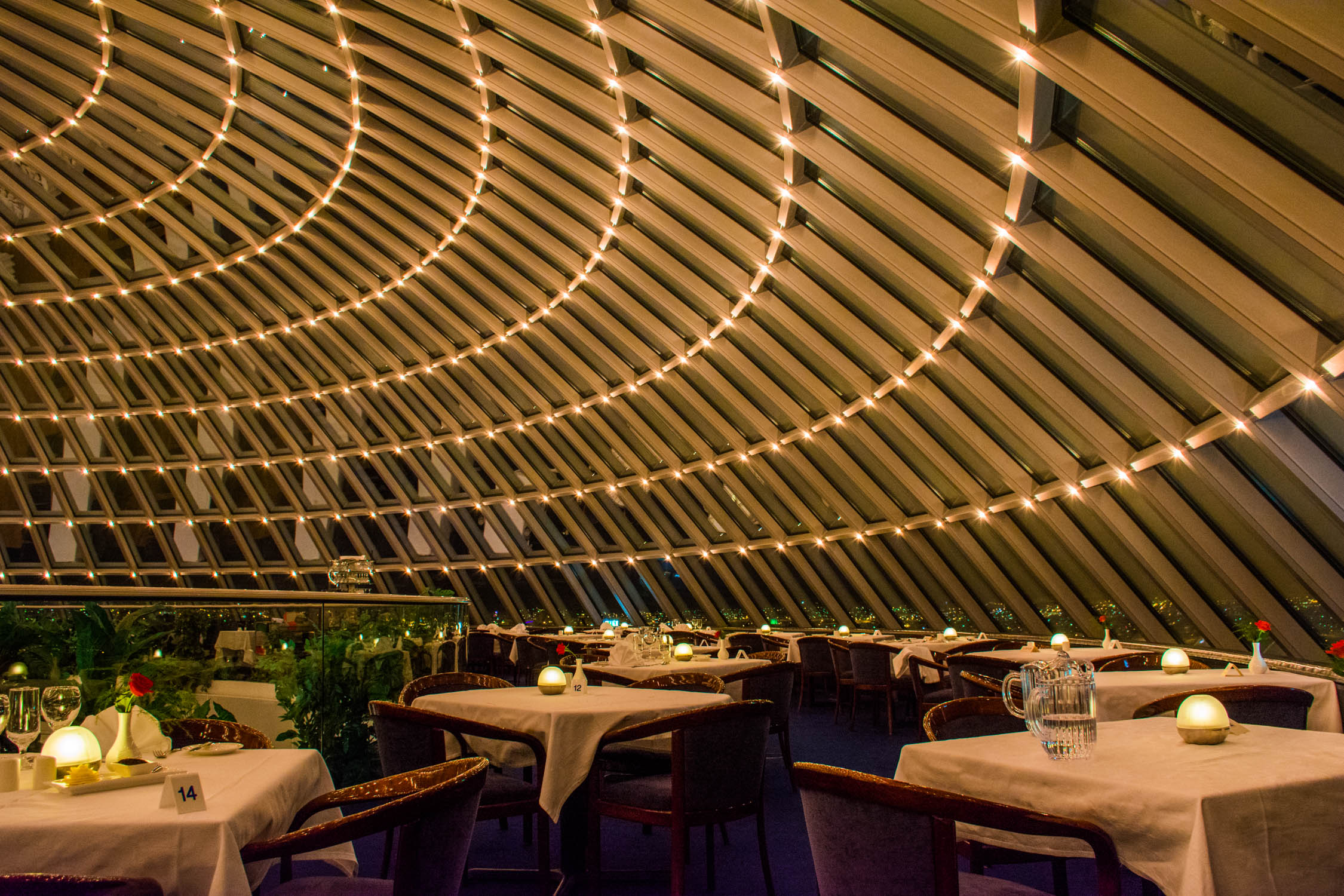 Tables set with white linens and candles under a curved wooden ceiling decorated with rows of small glowing lights.