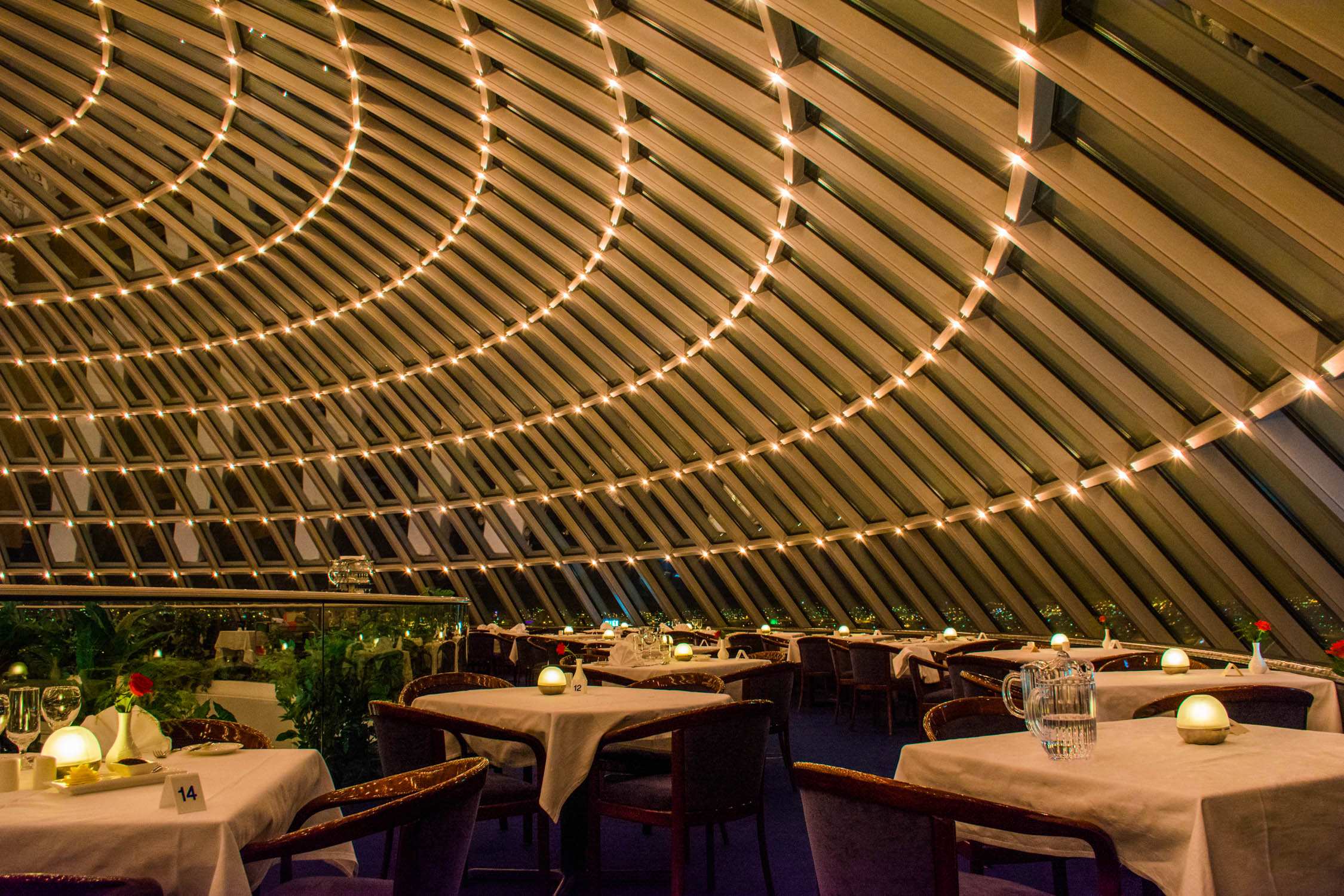 Tables set with white linens and candles under a curved wooden ceiling decorated with rows of small glowing lights.