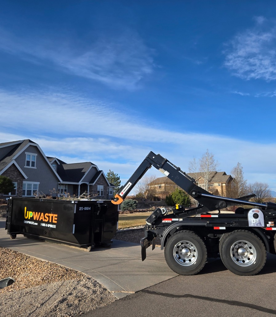 Partially built wooden house with construction materials stacked and UpWaste dumpster container in front