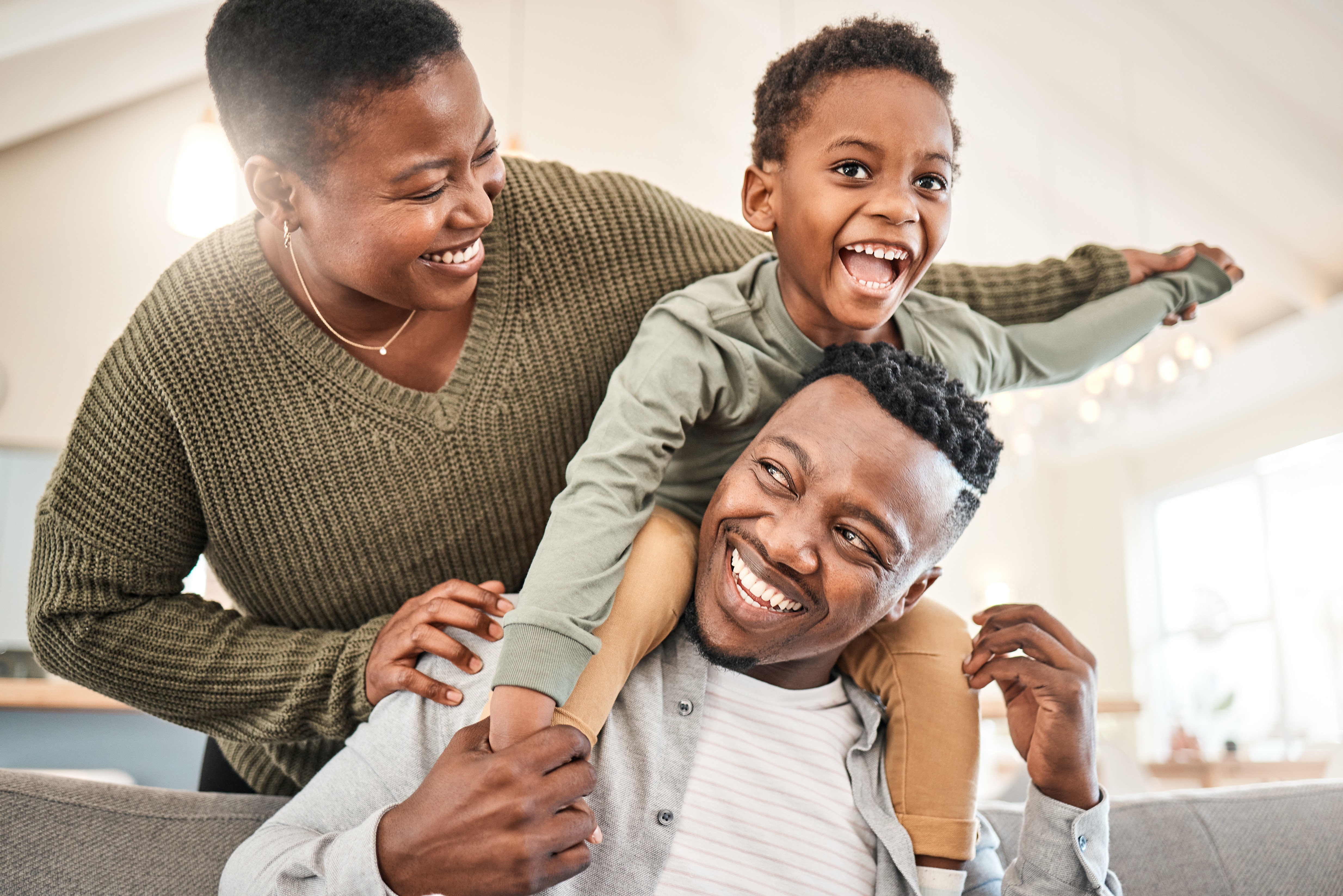 Laughing boy riding on his father's shoulders while his mother smiles beside them
