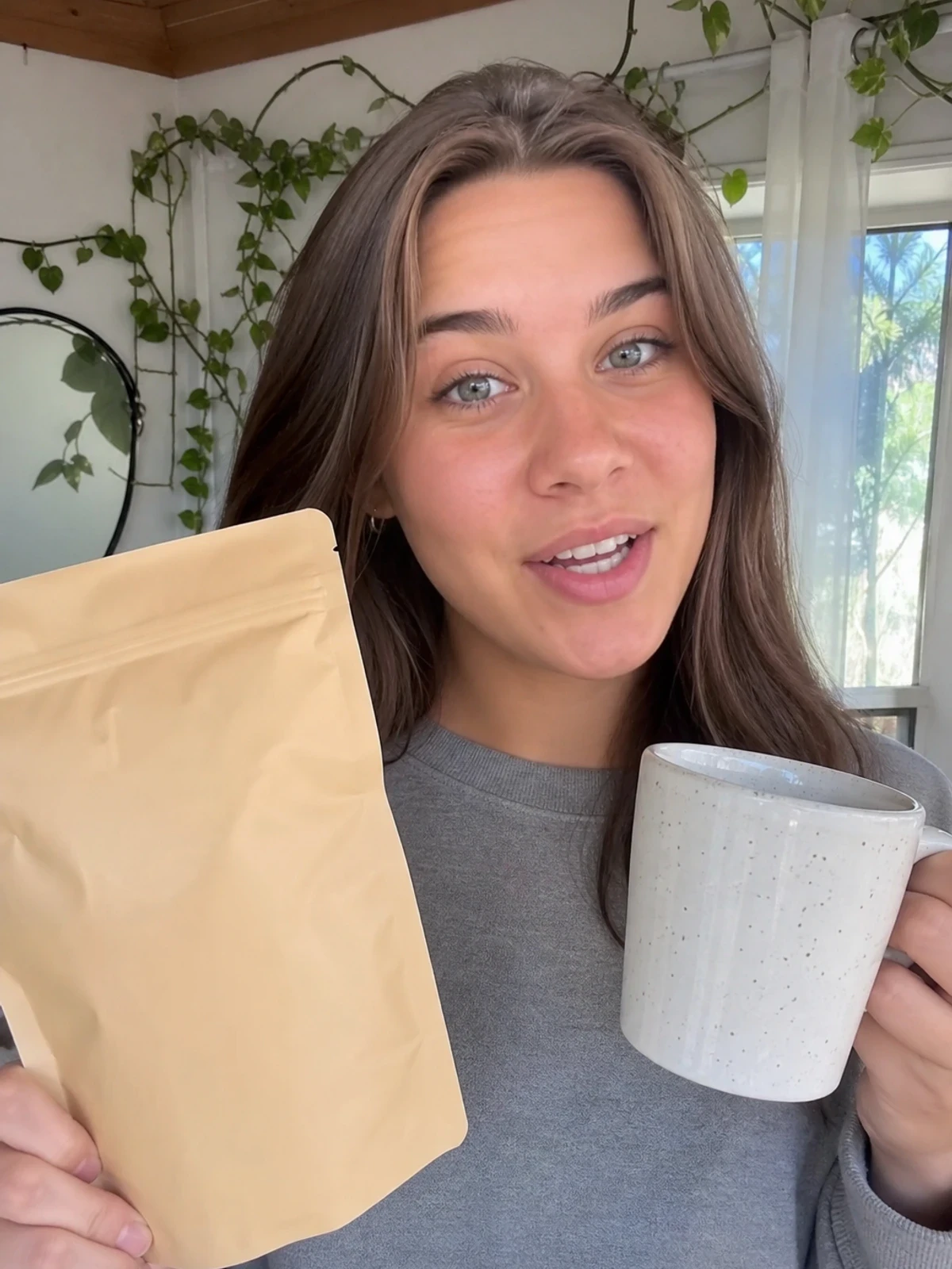 UGC-style photo: student creator, in a bright home studio, showing a coffee pouch and mug while talking to camera, close vertical talking-head shot.