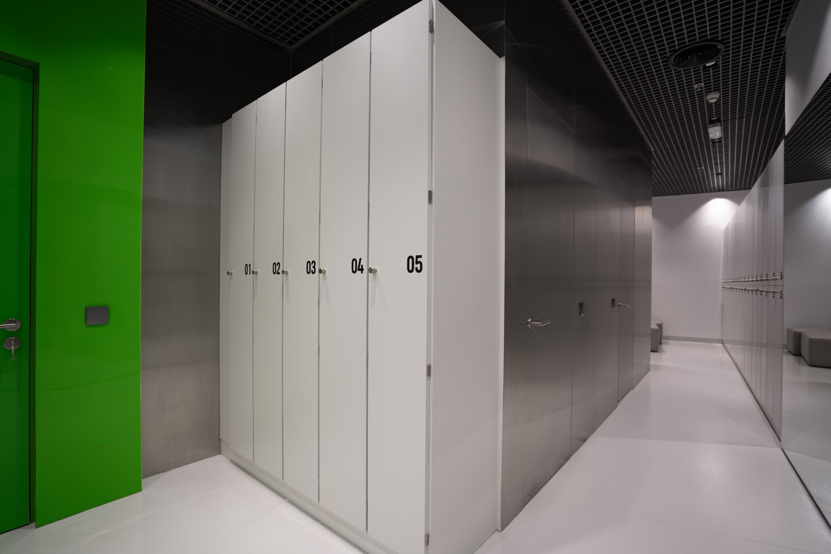 A sleek, modern locker room features white lockers with numbers, a vibrant green wall, and a dark, reflective ceiling, creating a minimalist and stylish atmosphere.