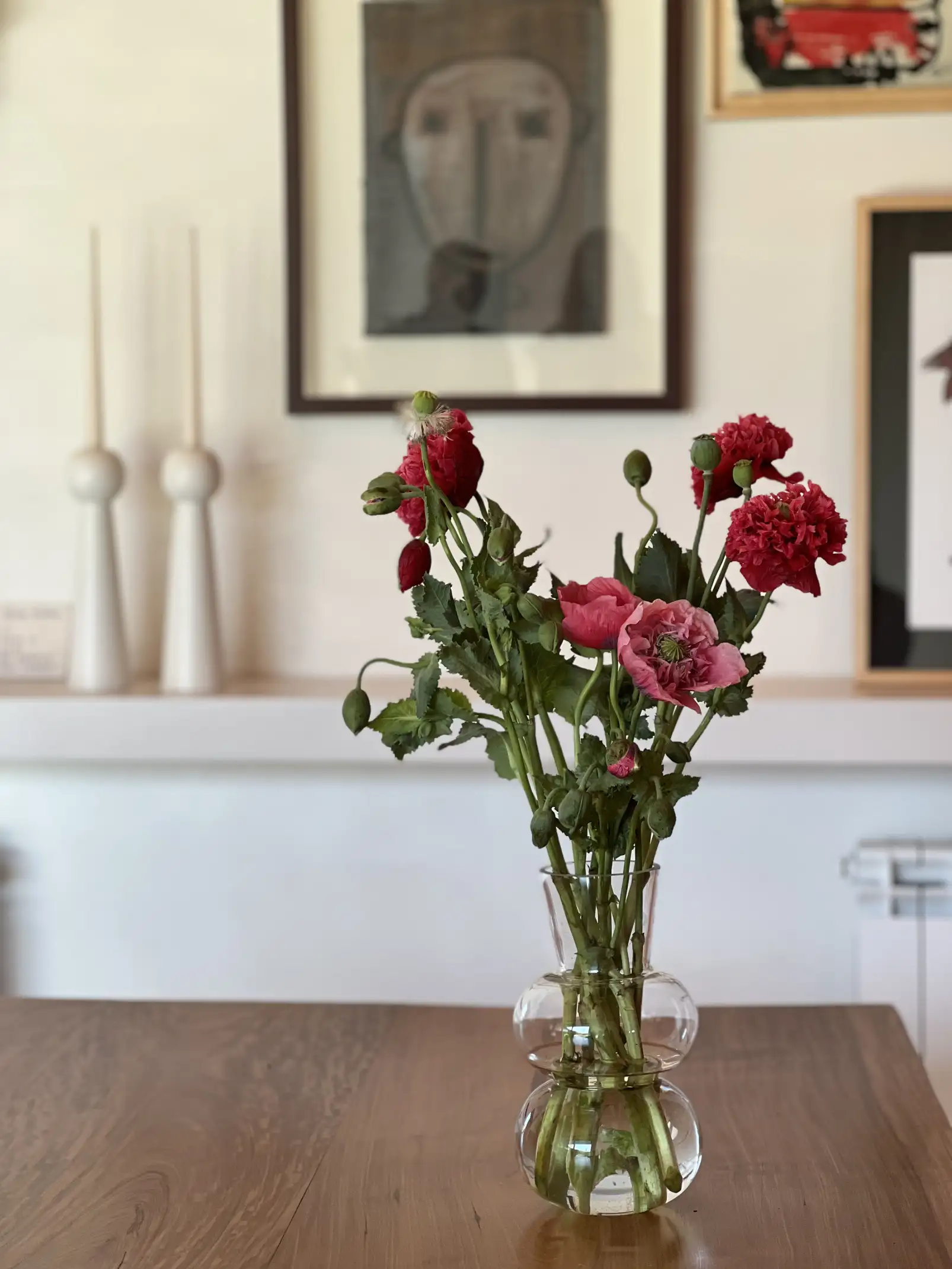 Detalle de flores rojas en jarrón de vidrio sobre mesa de madera para estilistas de interiores que destacan color y frescura natural.