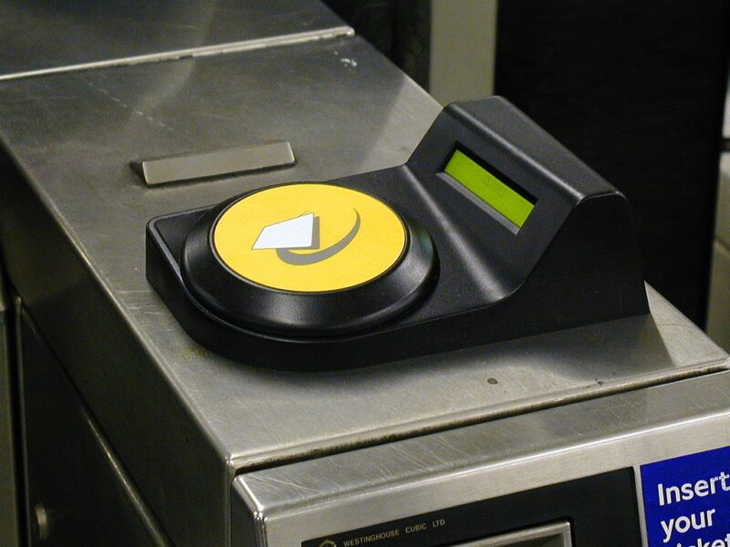 A yellow oyster card reader on a train station barrier.
