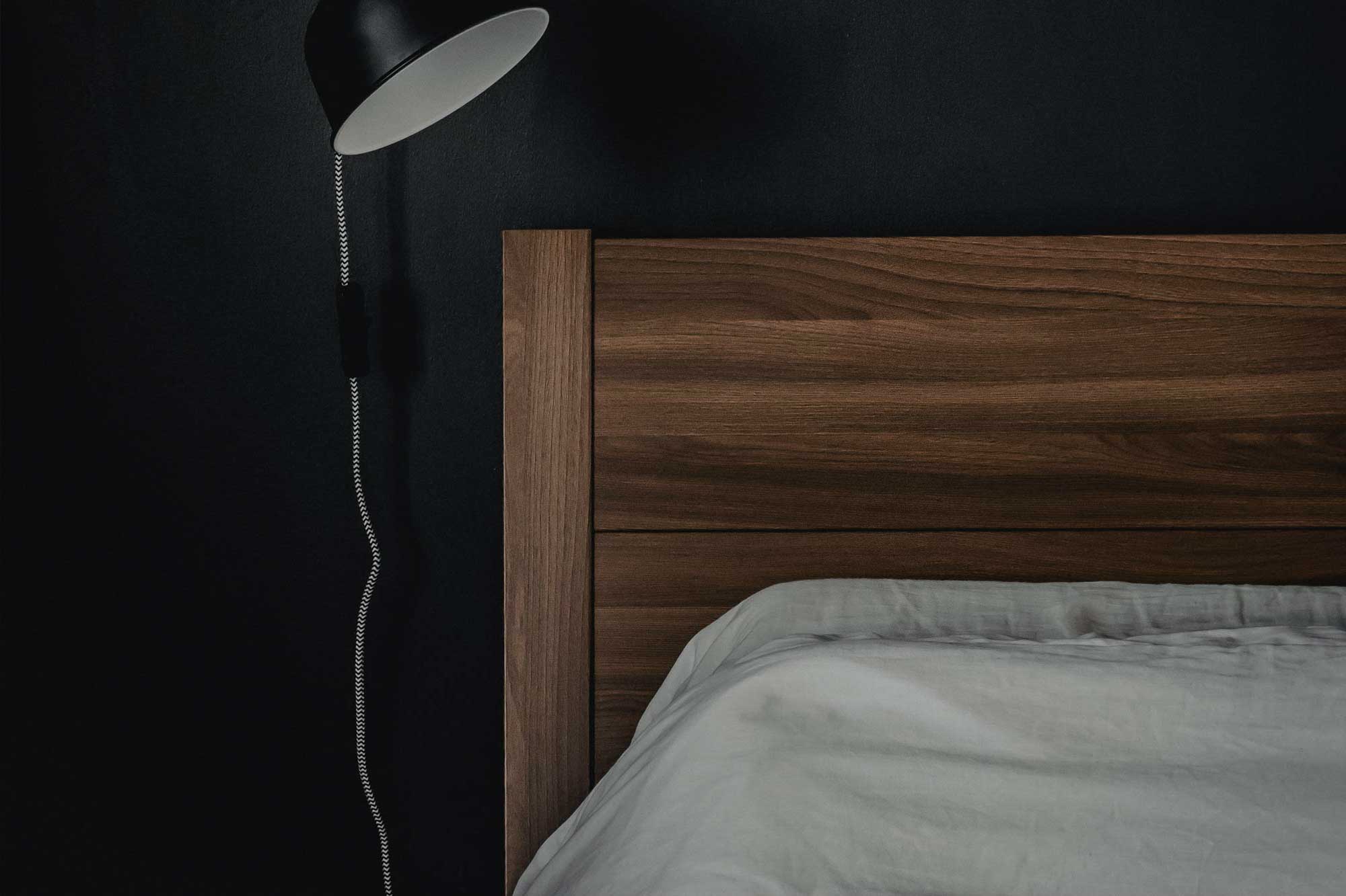 Wooden headboard and white bedding against a dark wall with a hanging bedside
