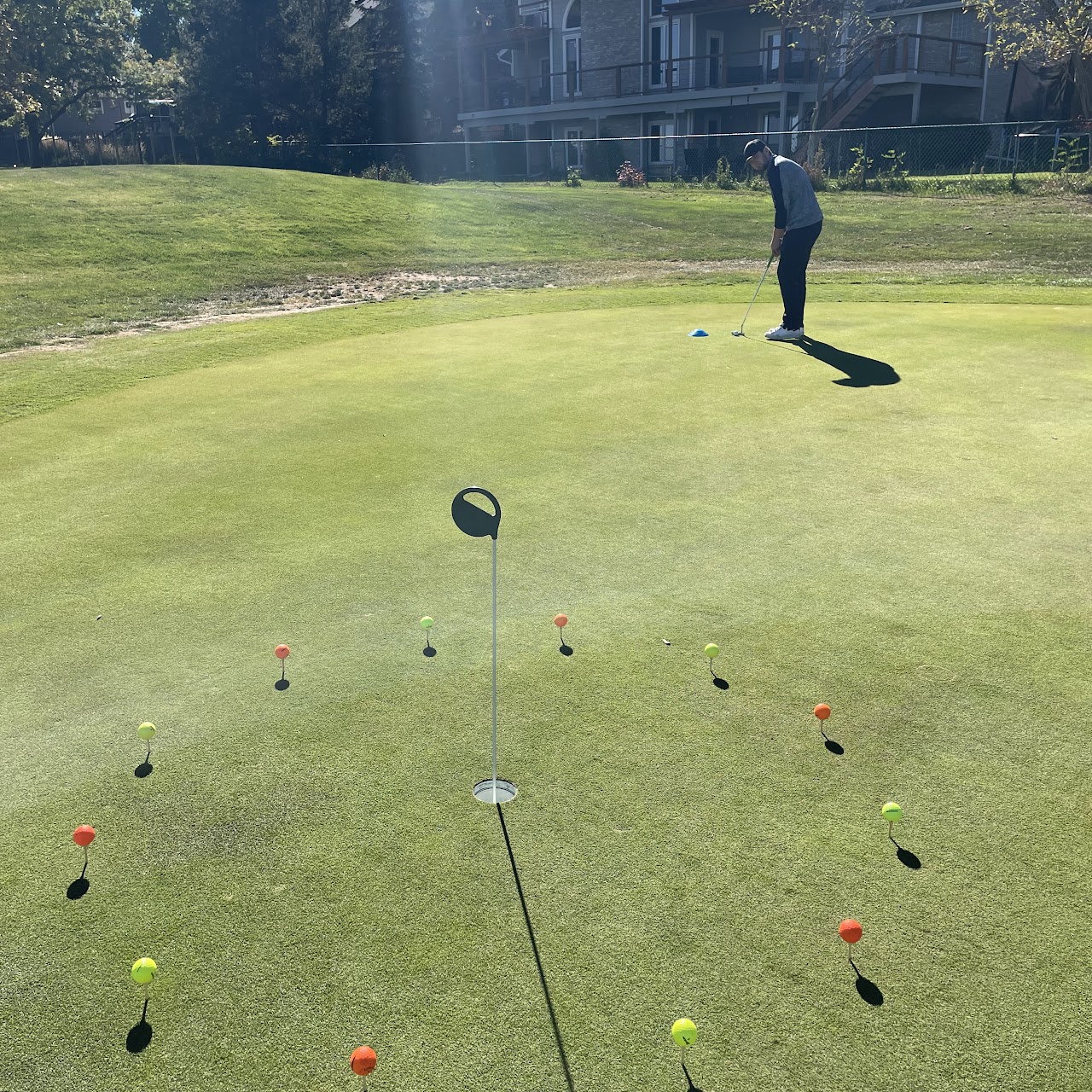 A man running through a putting drill on the green, with balls lined up on tees in a circle surrounding the cup.