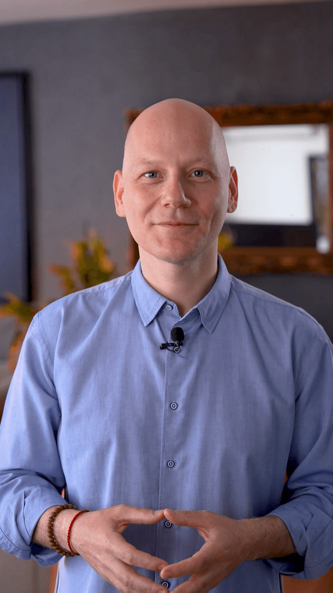 A young person with curly hair smiles at the camera while sitting in front of a laptop against a dark background.
