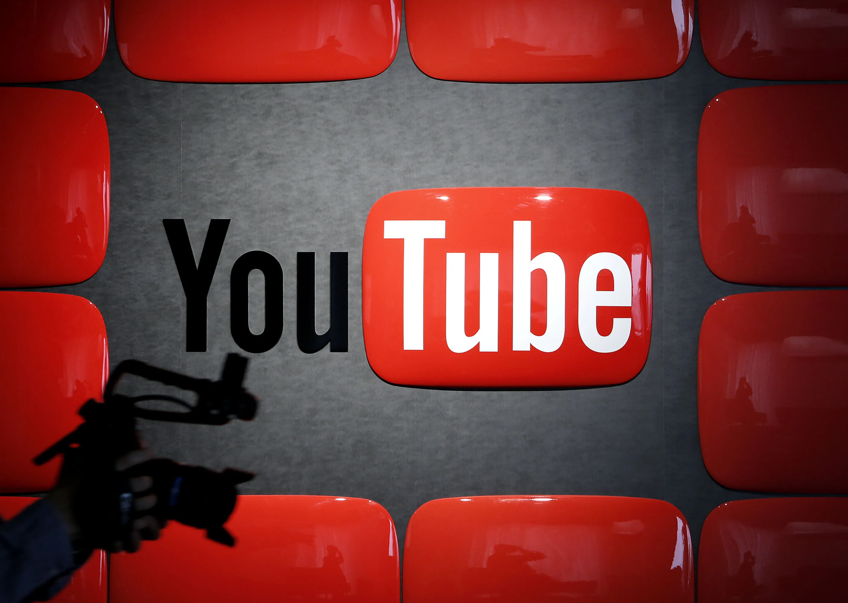 YouTube’s logo is displayed on a background with large red play buttons, featuring a silhouetted figure holding a camera in the foreground.