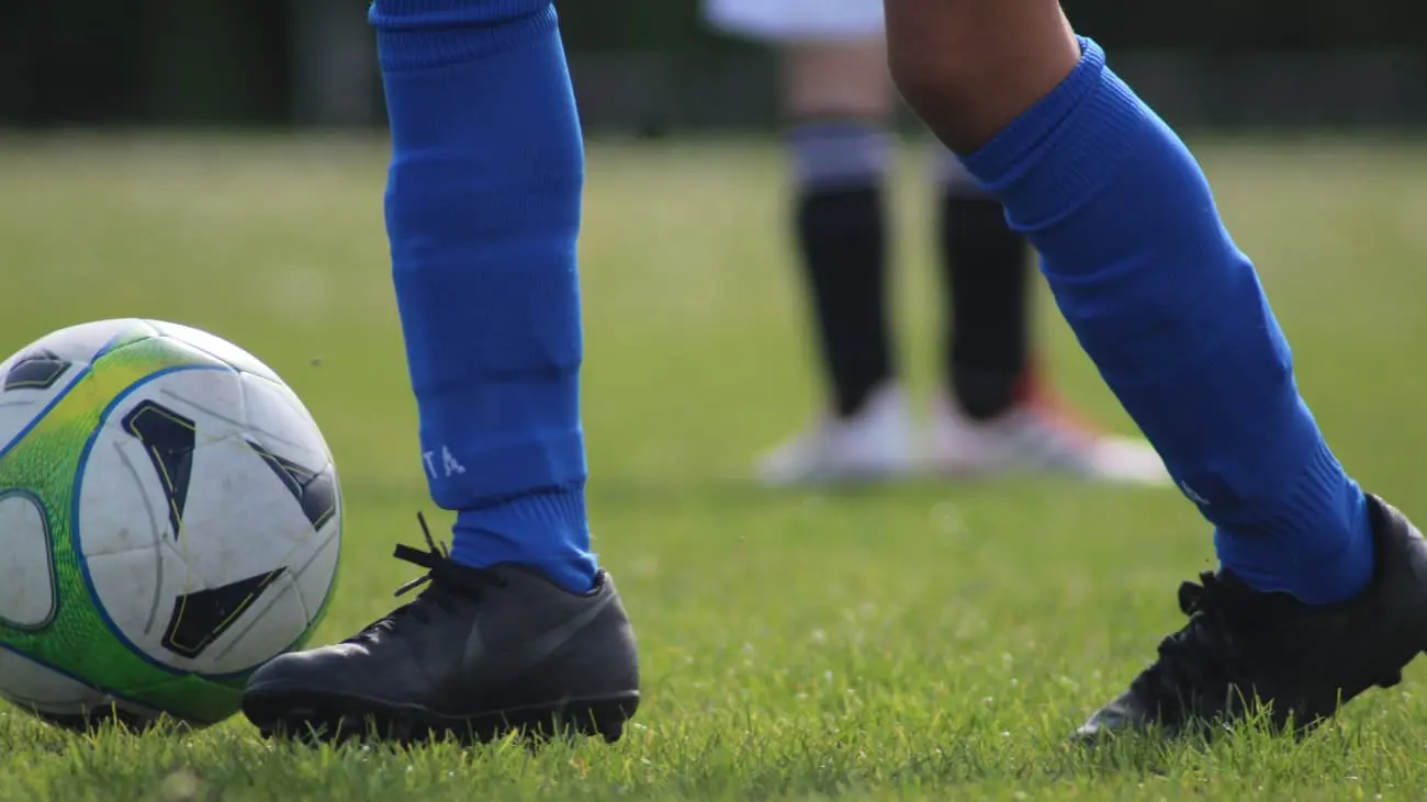 Discover the essence of youth football with this high-definition photograph vividly details the critical moment of a footballer's deft touch on the ball, poised for the game-changing pass. Adorned in striking blue socks and sleek black boots, the player is a standout against the perfectly maintained green pitch, illustrating the intense focus and finesse that define the beautiful game. We want to bring the spirit of the game closer to our readers. Immersing our audience in the world of football coaching with imagery that conveys the skill and dedication at the heart of the sport.