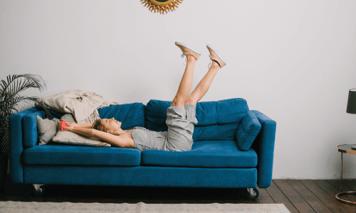 Frau entspannt auf blauem Sofa mit ihren Beinen in die Luft gestreckt