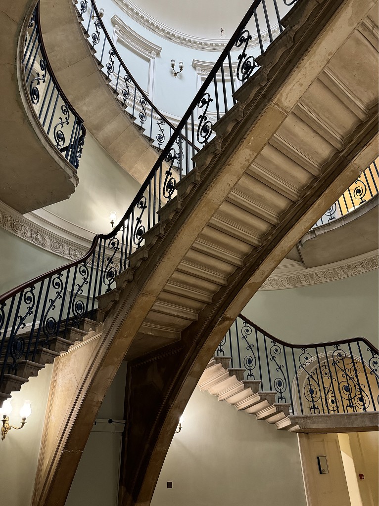 Interior stone staircase with wrought-iron balustrades in a historic building in UK, symbolising layered governance, structured decision-making, and long-term continuity.