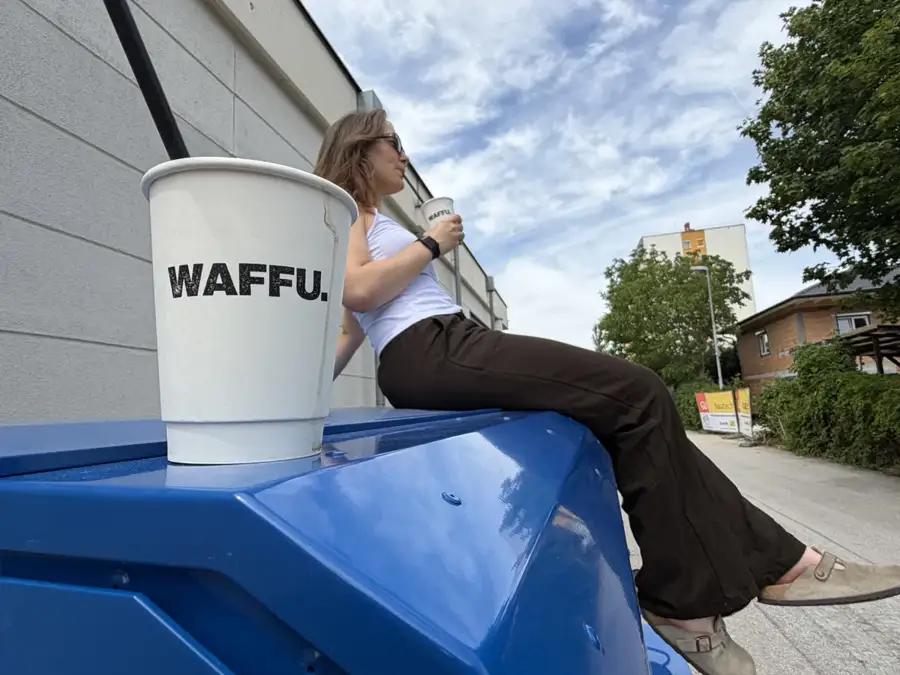 WAFFU Kaffeebecher auf der blauen Ape, im Hintergrund ein Gast