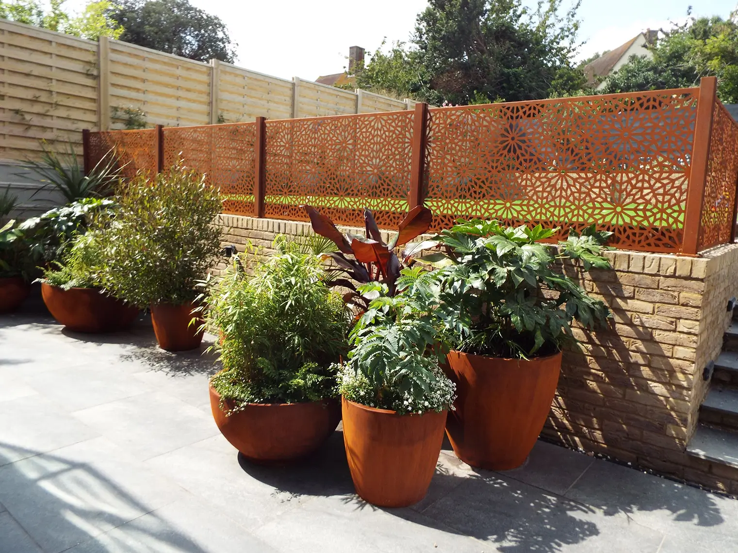 A sunny garden with several potted plants, surrounded by a wooden fence and a stone path.