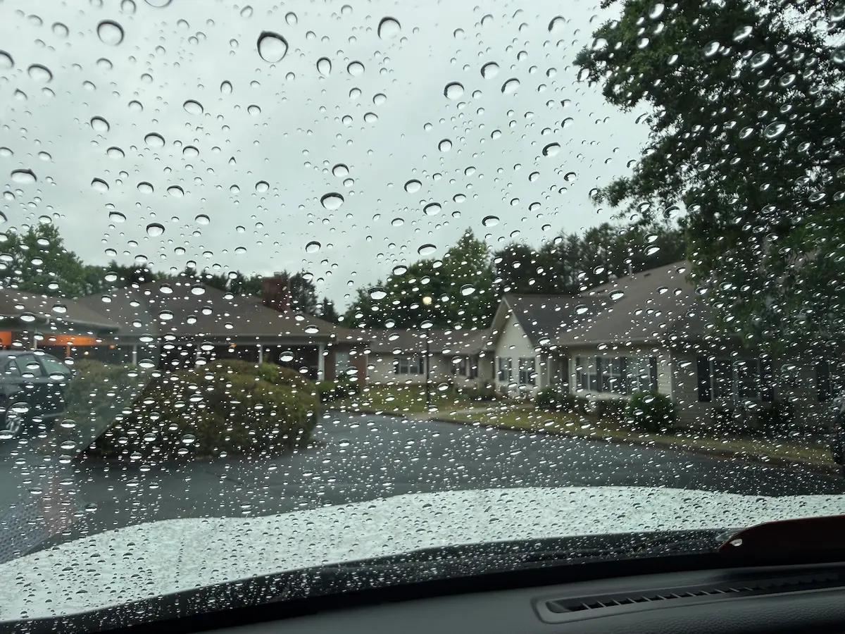 Raindrops on a car windshield looking out at a quiet residential street