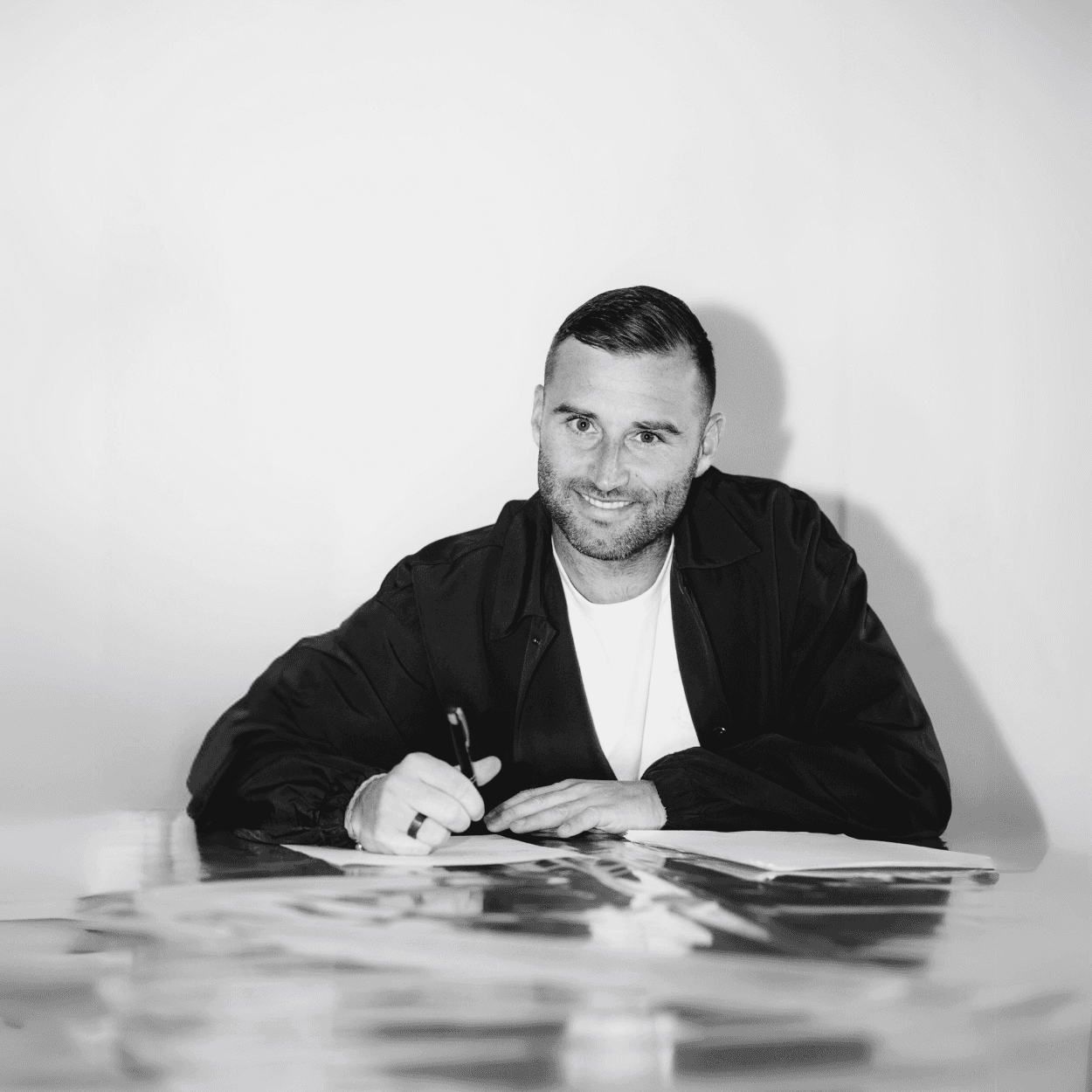 Portrait of Tuur Dierckx, founder of The Labyrinth, seated at a table, smiling confidently while working on project plans. The monochromatic image highlights his professional yet approachable demeanor