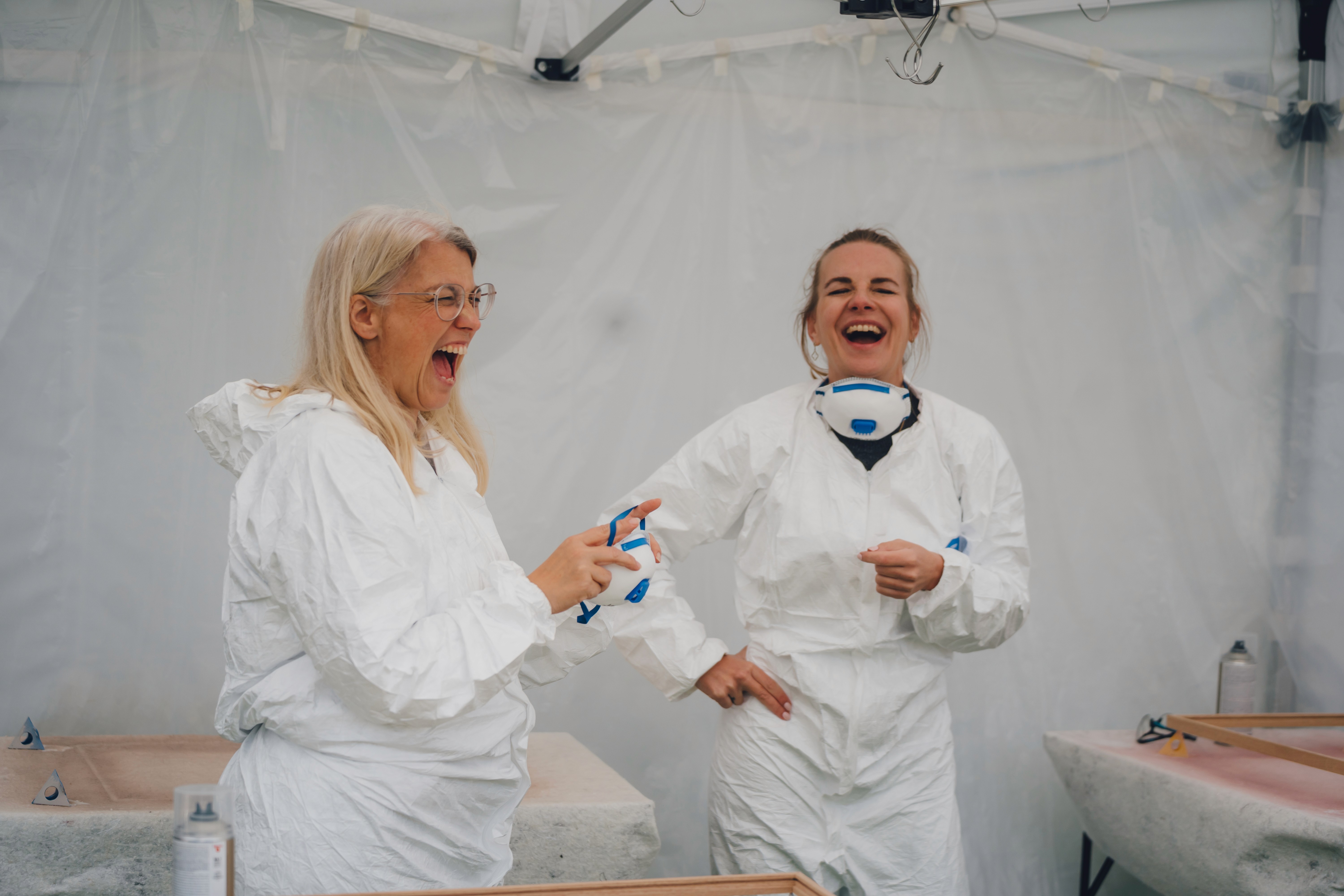 Zwei Frauen lachen während eines DIY-Workshops mit Schutzanzügen in einem Kreativzelt