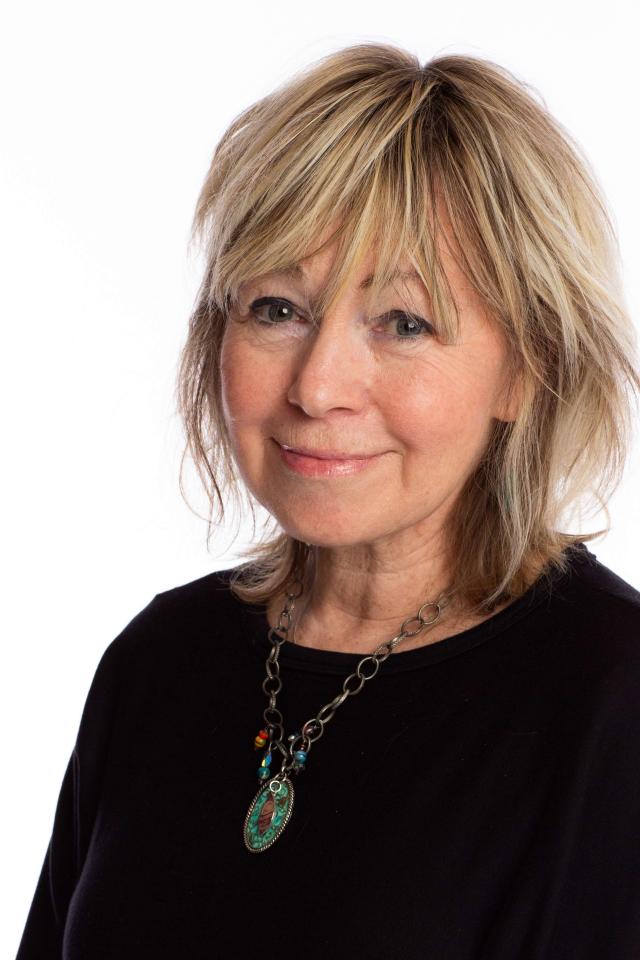 Smiling woman with short blonde hair and a necklace, looking at the camera.