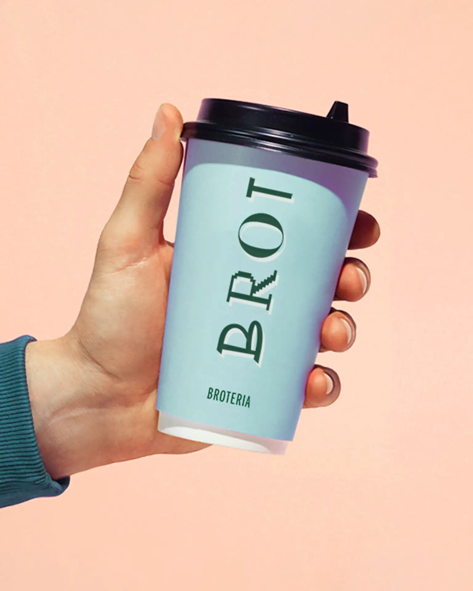 Hand holding a light blue Broteria takeaway coffee cup with green typography