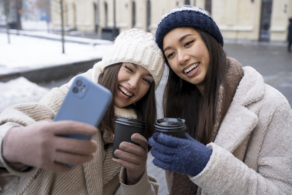 female friends taking selfie holding coffee cups outdoors winter