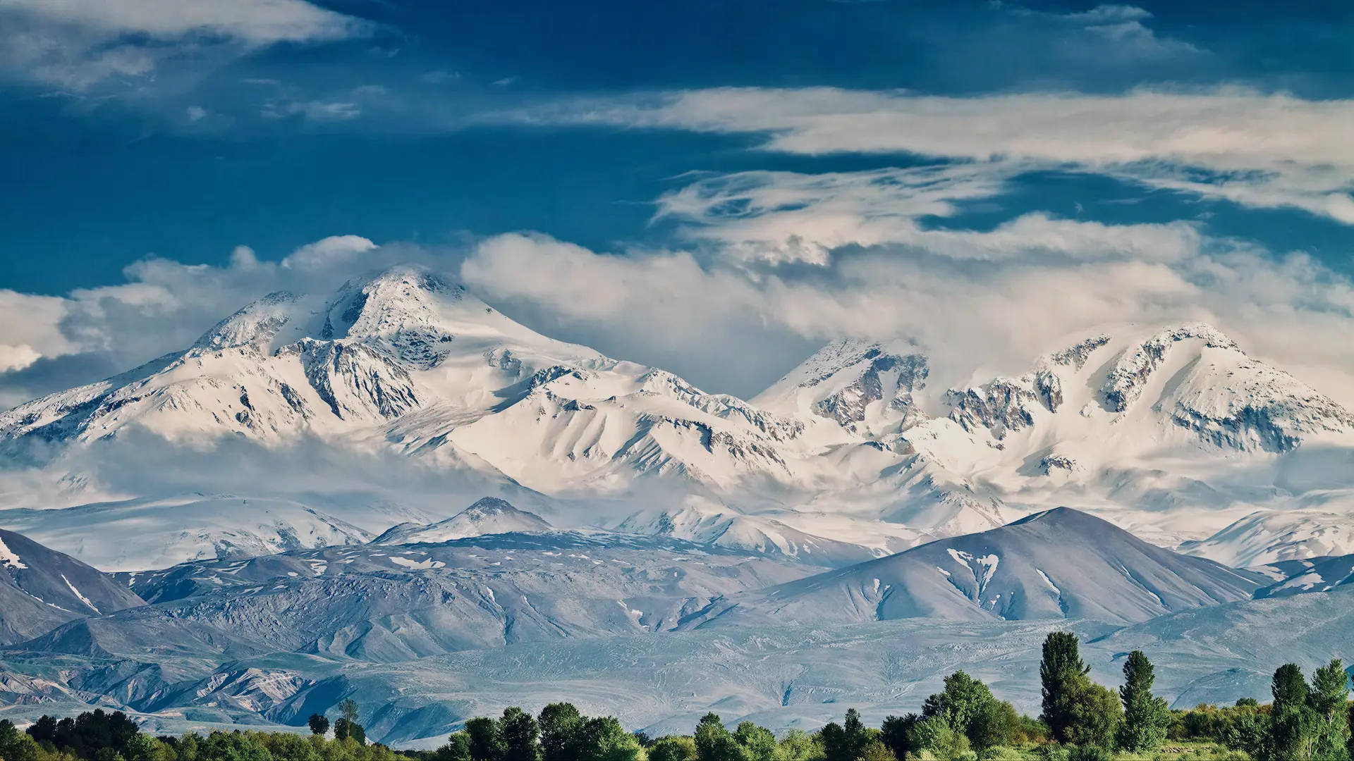 Snow-capped Zagros Mountains rising above foothills and green treeline in northern Iraq