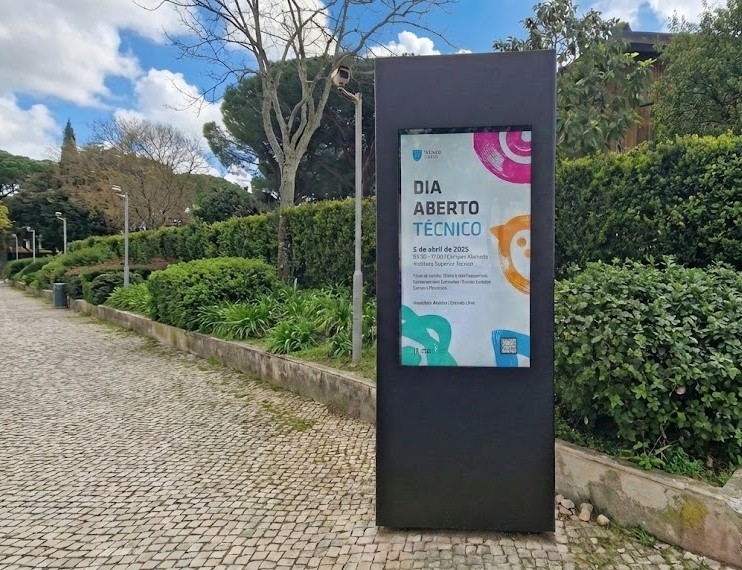 Totem digital exterior a exibir o cartaz do evento "DIA ABERTO TÉCNICO" para 5 de abril de 2025.
