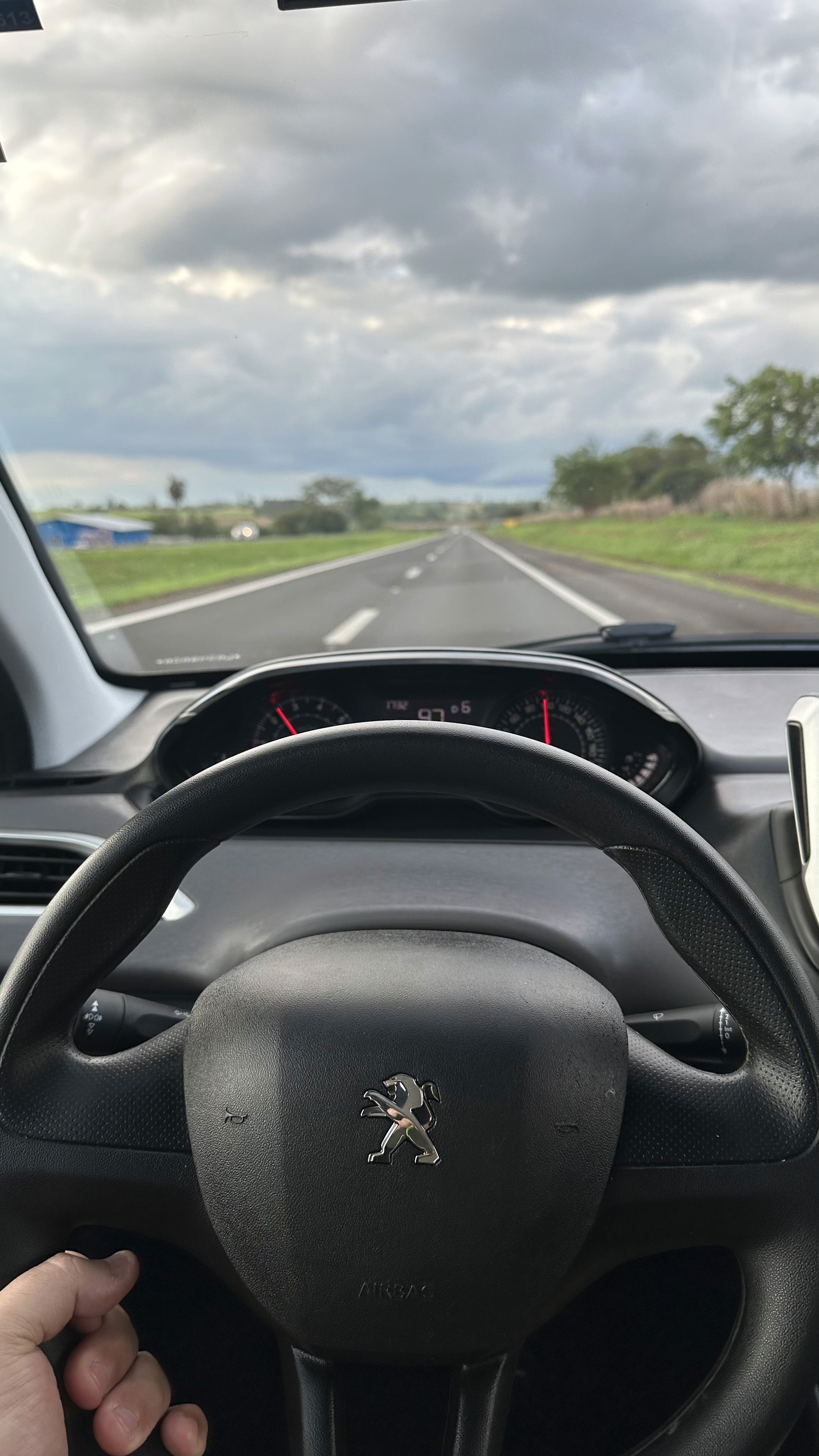 As mãos de Will no volante, com a visão de uma estrada aberta e um céu nublado à frente.