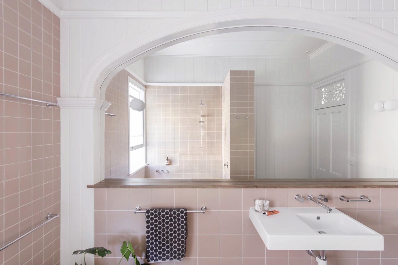 Bathroom interior with pink tiled walls, arched opening, wall-mounted sink, and walk-in shower