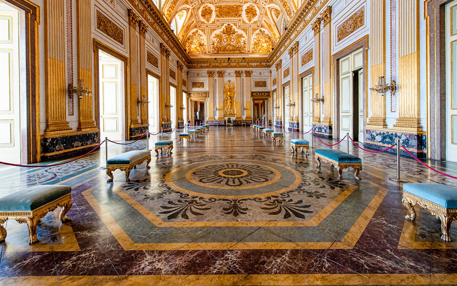 Interior del Palacio Real de Caserta con techo ornamentado y piso de mármol.