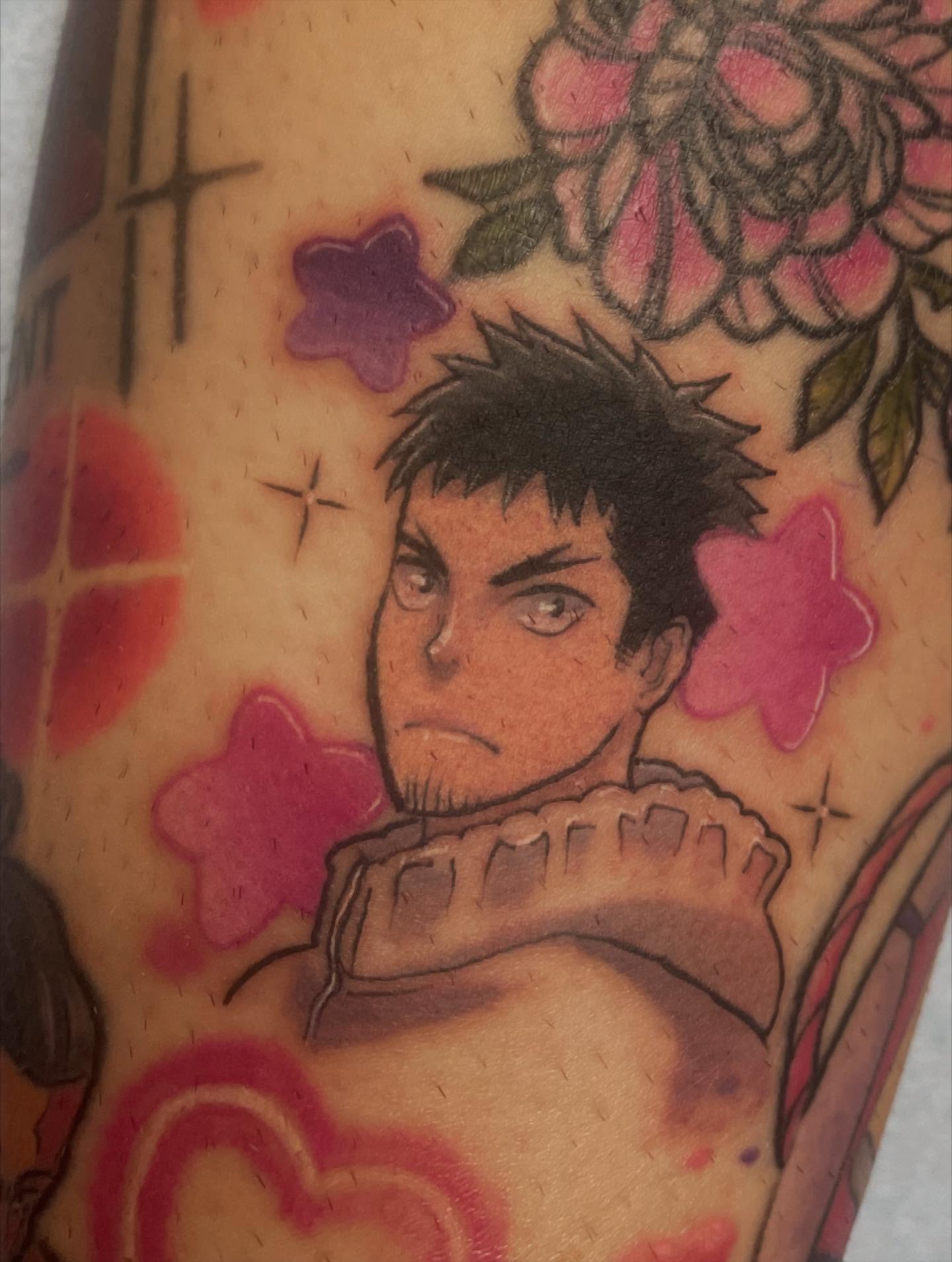 A vibrant tattoo of a chainsaw-like creature on a person's forearm. The tattoo is detailed with shades of orange, black, teal, and red.