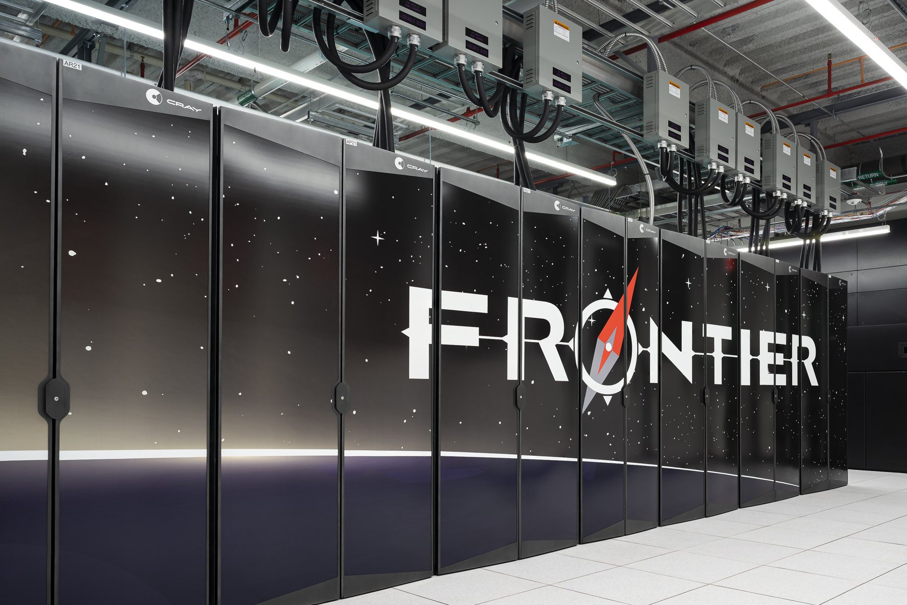 A row of black Frontier supercomputer cabinets beneath overhead power and cooling infrastructure.