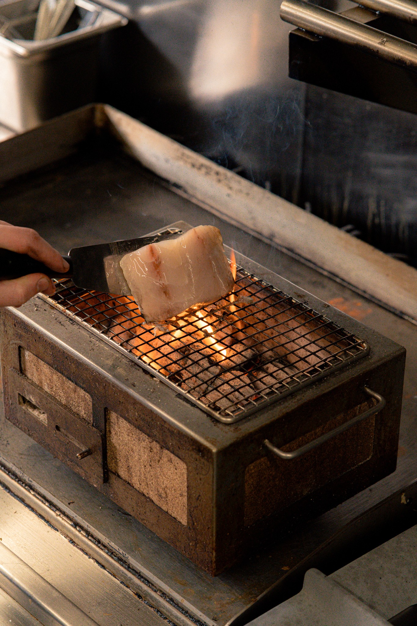 cuisson d’un morceau de viande sur un gril au charbon, mettant en valeur les techniques culinaires du chef et la qualité des produits.