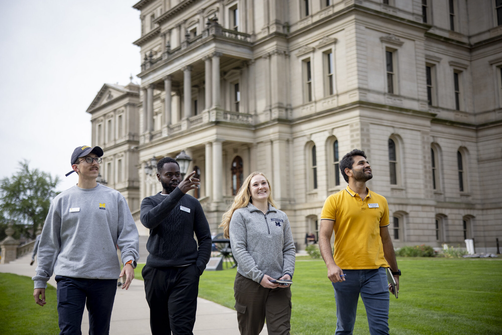 Four people walking together on a pathway in front of a historic building. Green lawn surrounds them.