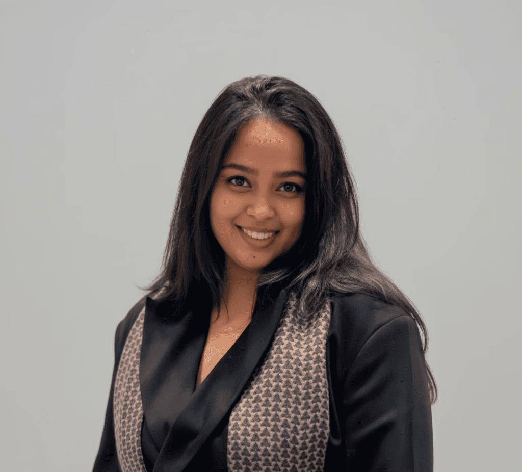 Professional headshot of a brunette woman in a white shirt, arms crossed, on a clean minimal background.