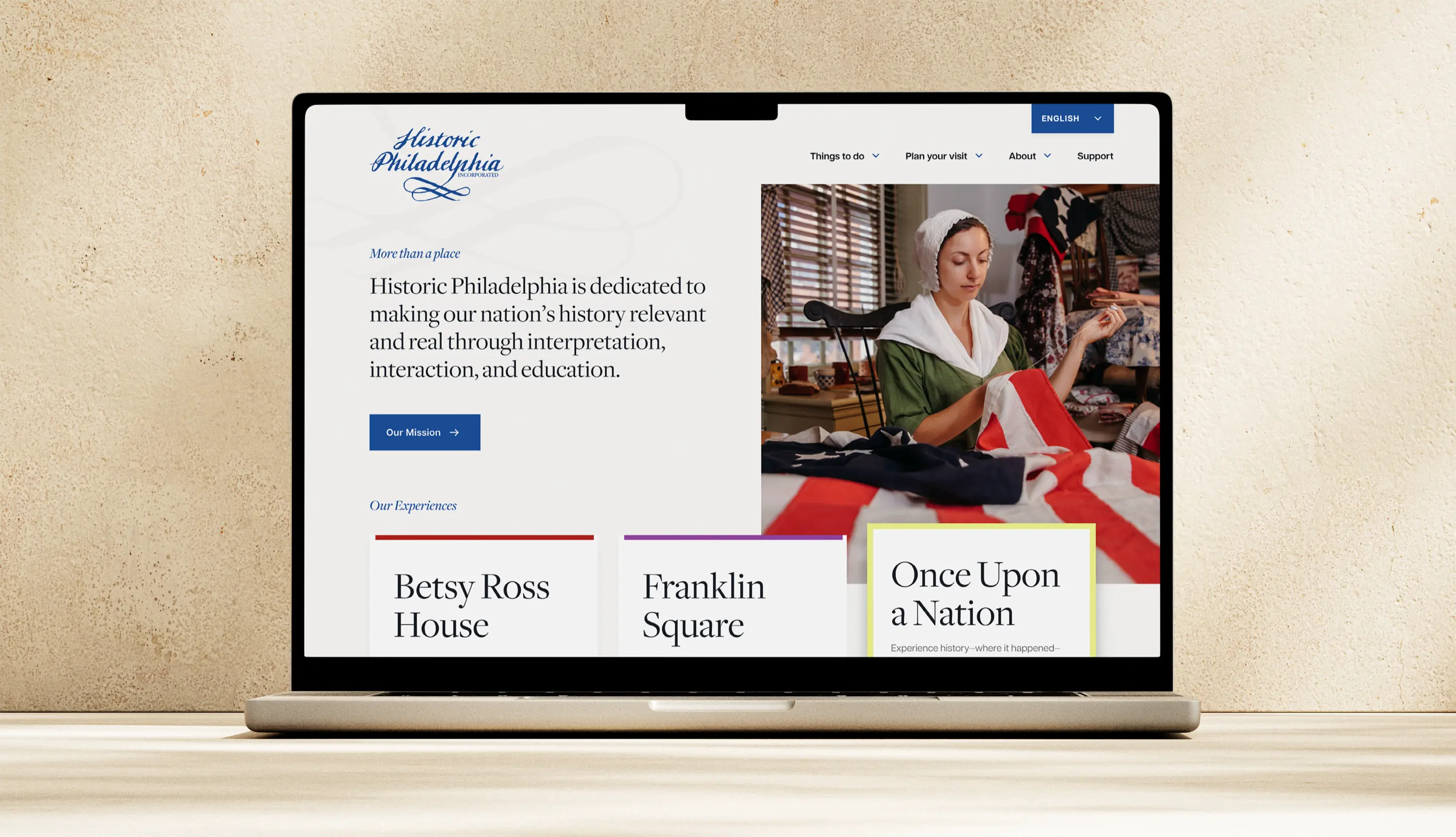 Historic Philadelphia homepage design shown on laptop, featuring a Betsy Ross reenactor and multilingual language toggle