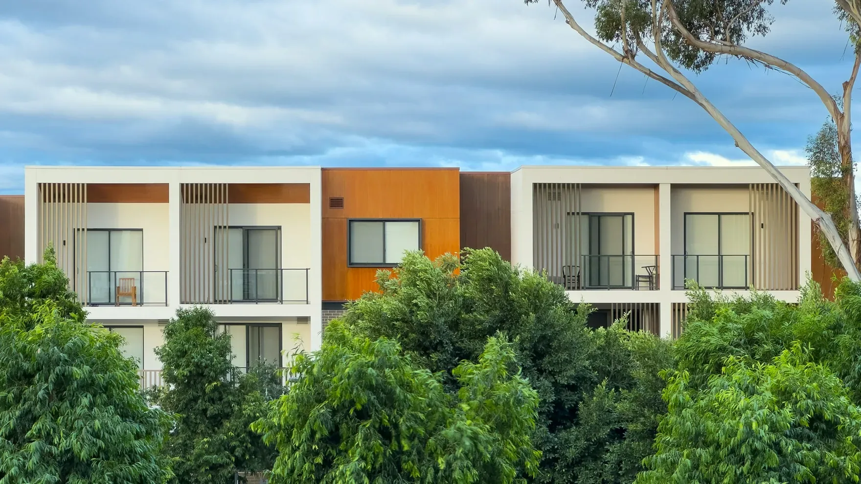 Low-rise condo building with balconies behind green trees