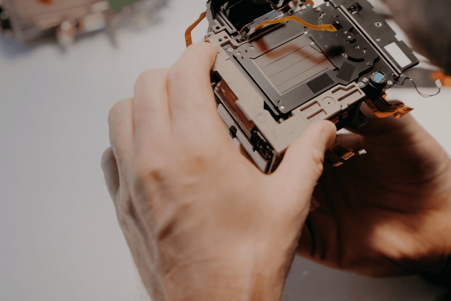 Close-up of hands repairing a digital camera, showing internal components and wiring.