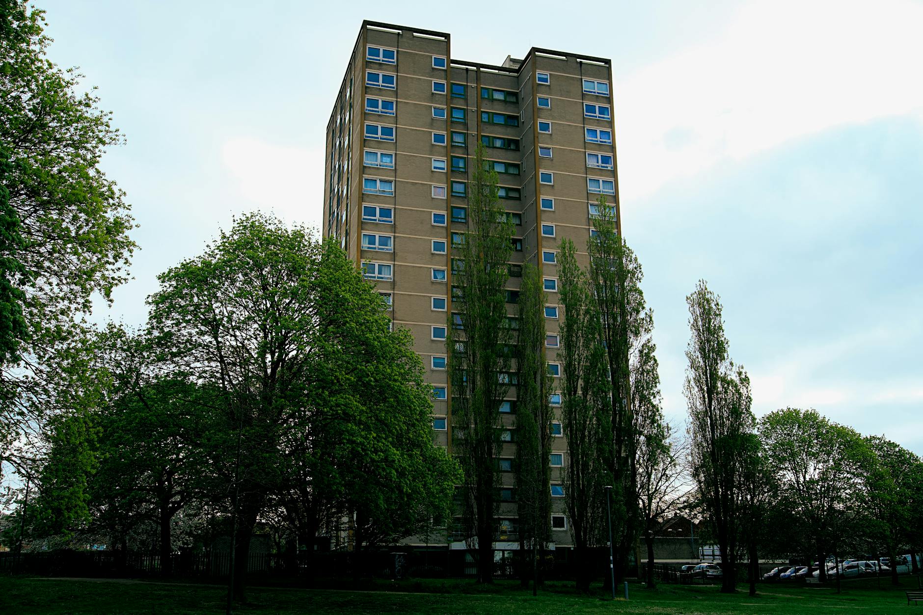 Tall 1970s concrete tower block surrounded by mature trees against a grey sky