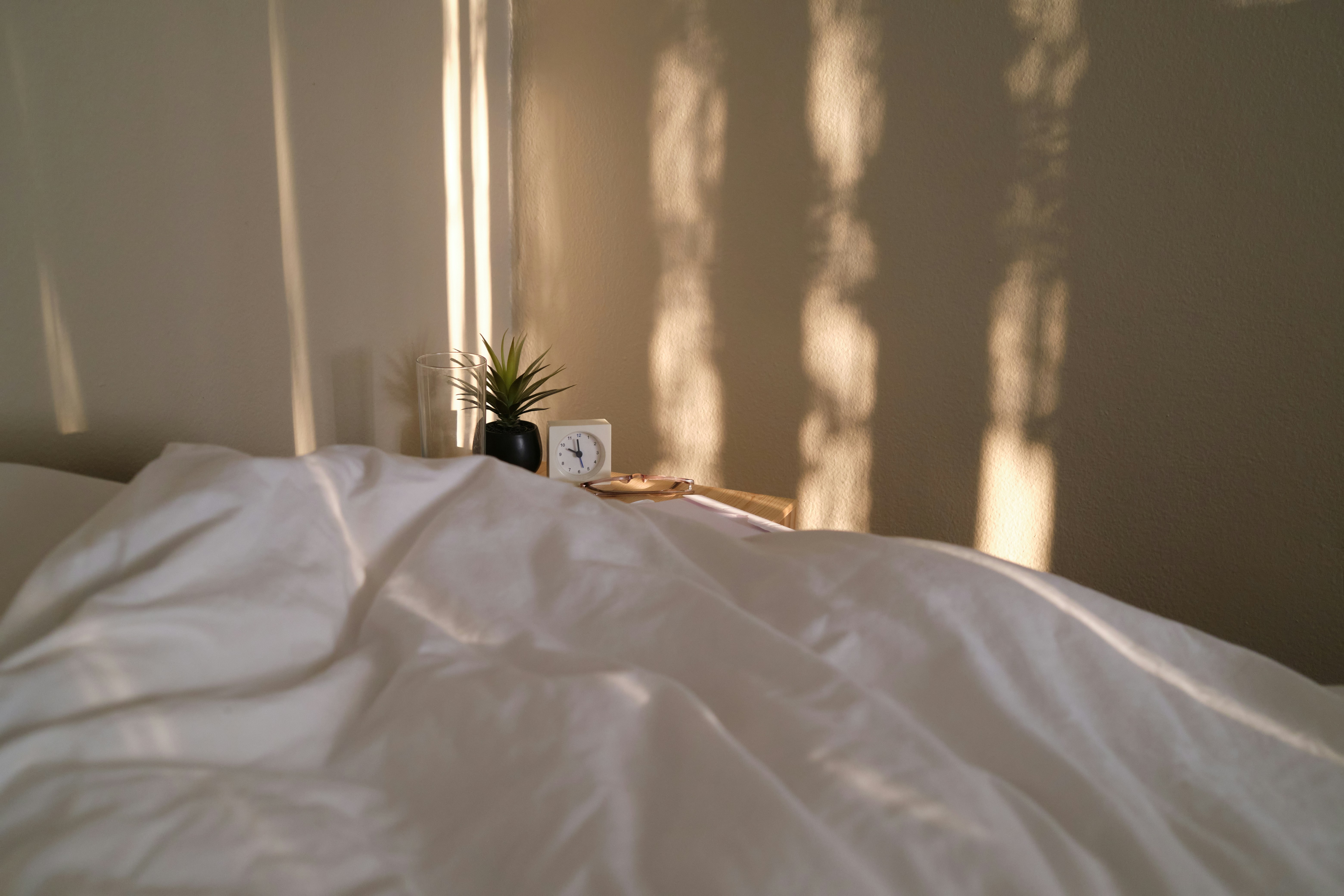 a bed with a white comforter and a plant on top of it