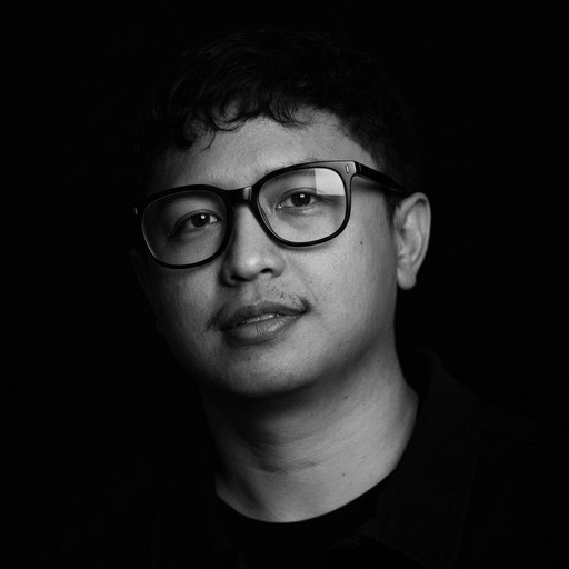 Person wearing a blue puffer jacket and red backpack standing in front of a light blue building on a city street.