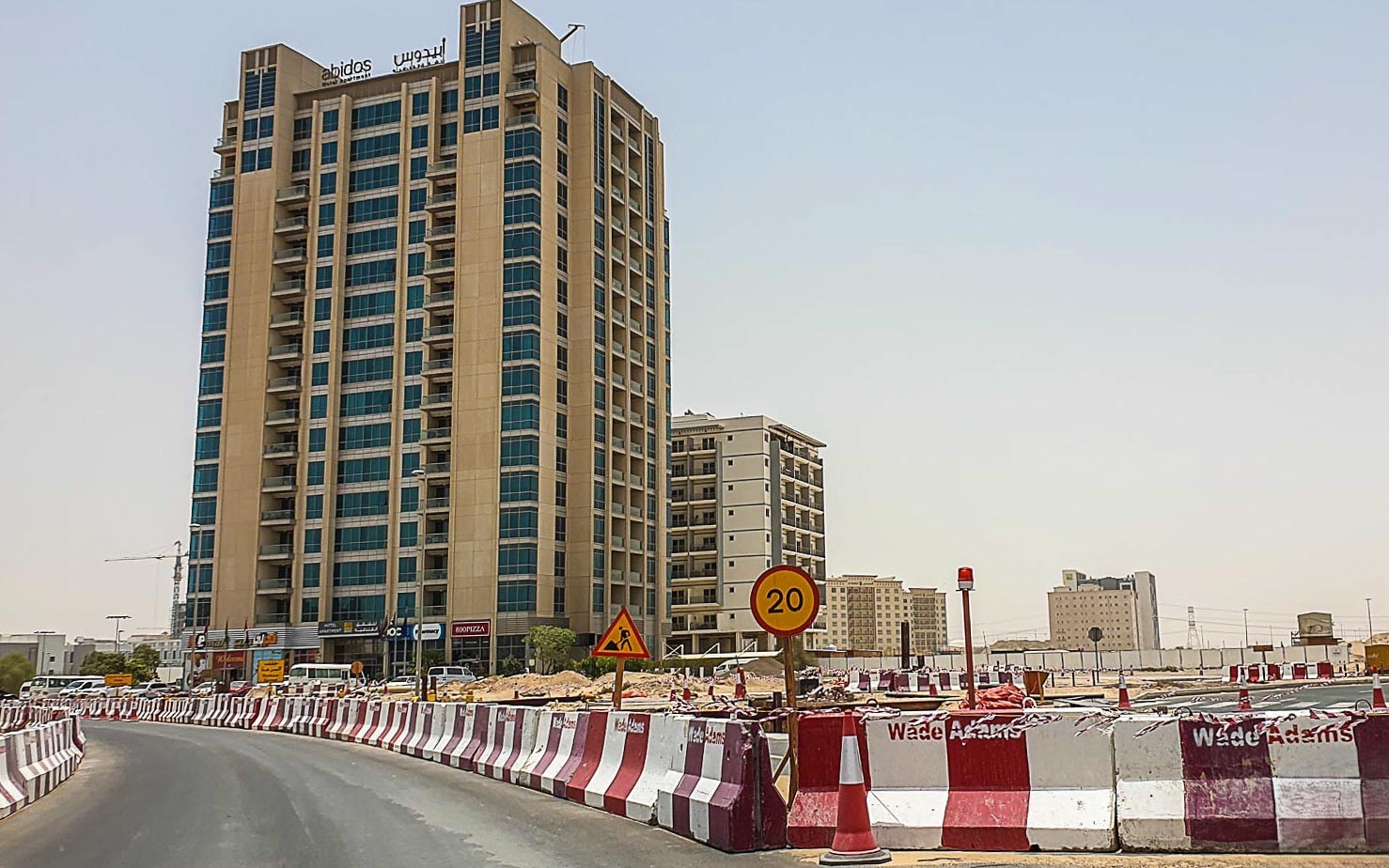 Aerial view of a modern high-rise apartment building with a pool in Dubailand Residence Complex, surrounded by greenery.