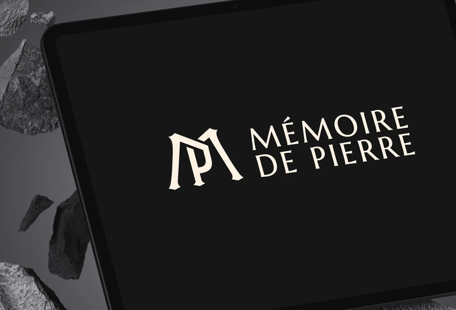 Logo Mémoire de Pierre affiché sur une tablette posée parmi des pierres